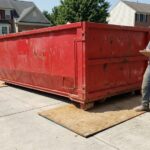 Contractor reviewing a dumpster permit in Montgomery County, MD next to a red roll-off bin.
