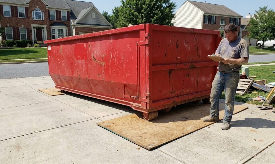 Contractor reviewing a dumpster permit in Montgomery County, MD next to a red roll-off bin.